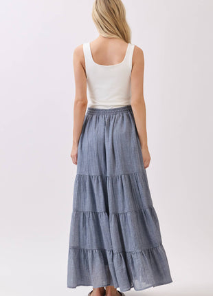Woman wearing a white top and blue tiered skirt on a plain background