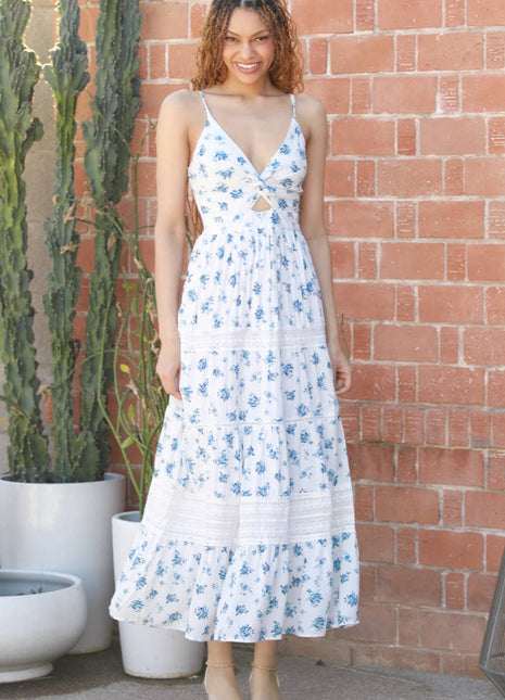 Woman wearing a white floral dress standing against a brick wall with cacti in the background.