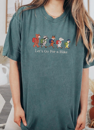 Woman wearing a teal t-shirt with cartoon characters and text, standing in a room with decor.