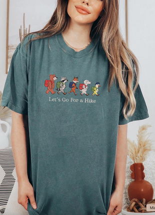 Woman wearing a teal t-shirt with cartoon characters and text, standing in a room with decor.
