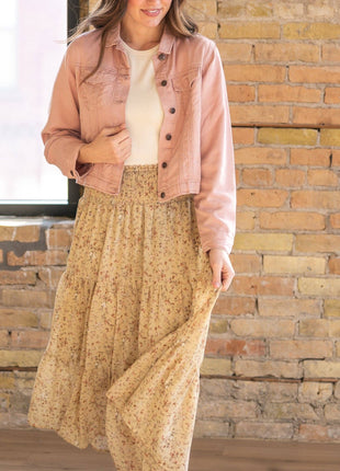 Woman wearing a pink jacket and beige skirt standing against a brick wall.
