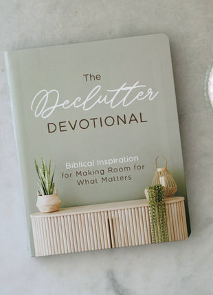 Book titled 'The Declutter Devotional' on a marble surface with decorative items.