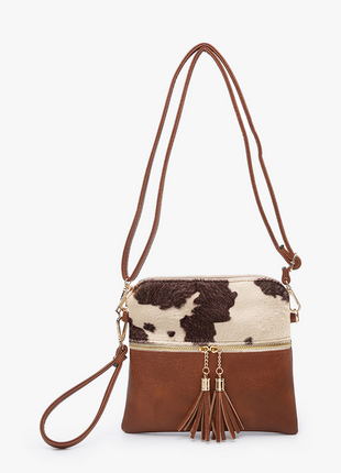 Brown and white cowhide crossbody bag with tassels on a light beige background