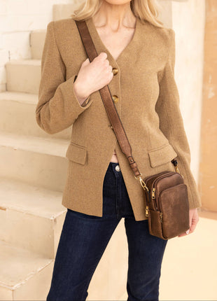 Woman in a beige blazer holding a brown leather bag on a staircase.