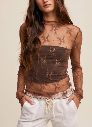 Woman wearing a sheer brown lace top with white pants on a beige background