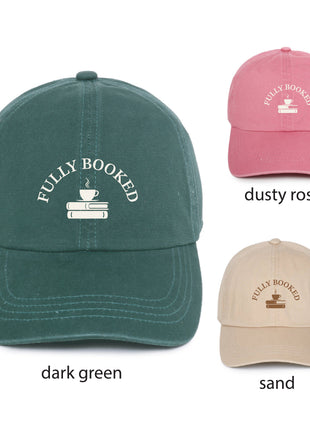 Three baseball caps shown on a white background with color labels: a large dark green cap labeled 'dark green,' a smaller dusty rose cap labeled 'dusty rose,' and a smaller sand cap labeled 'sand.' Each cap has white embroidered text reading 'FULLY BOOKED' above a small coffee cup and books graphic.