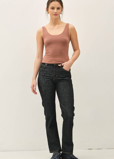 Woman wearing a brown tank top and black jeans against a white background