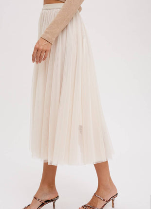 Beige pleated skirt worn with a beige top and leopard print sandals on a white background