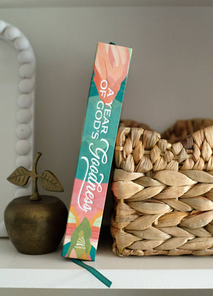 Colorful bookend with 'A Year of God's Goodness' text on a shelf with decorative items.