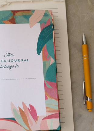 Prayer journal with colorful cover, pen, and cup on a light surface