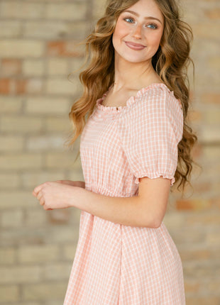 Woman wearing a pink dress standing against a brick wall.