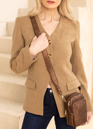 Woman in a beige blazer holding a brown leather bag on a staircase.