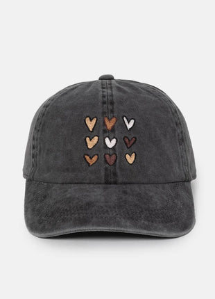 A dark gray washed cotton baseball cap featuring embroidered hearts in various colors (brown, beige, white, and reddish-brown) arranged in a grid on the front, set against a plain light gray background.