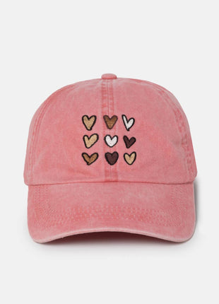 A pink washed cotton baseball cap featuring nine embroidered hearts in various colors (brown, beige, white, and dark brown) arranged in a 3x3 grid on the front panel.