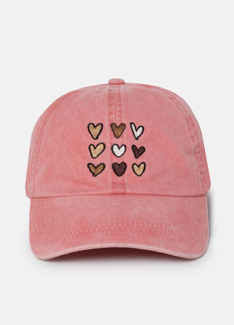 A pink washed cotton baseball cap featuring nine embroidered hearts in various colors (brown, beige, white, and dark brown) arranged in a 3x3 grid on the front panel.