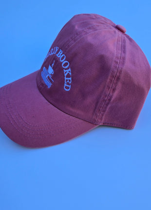 A pink baseball cap with white embroidered text reading 'NEW BORKED' and a small boat graphic, shown on a solid blue background.