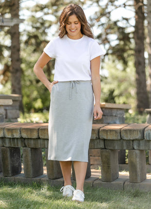 Woman wearing a white t-shirt and light gray skirt standing outdoors near stone benches.