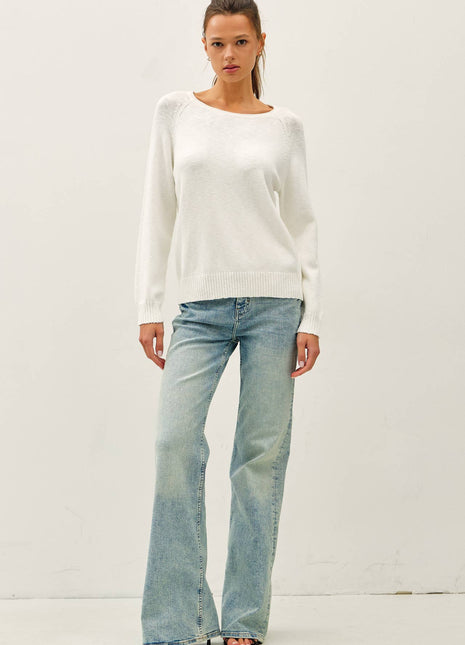 Woman wearing a white sweater and light blue jeans against a plain background