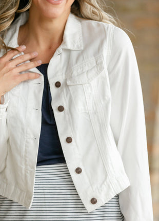 White denim jacket with brown buttons worn by a person, blurred background