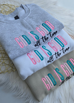 Two folded sweatshirts with colorful text design on a fluffy white surface.
