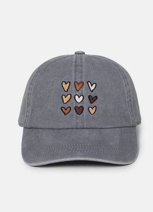 A gray washed baseball cap featuring a grid of embroidered hearts in various earthy tones on the front, set against a plain light gray background.