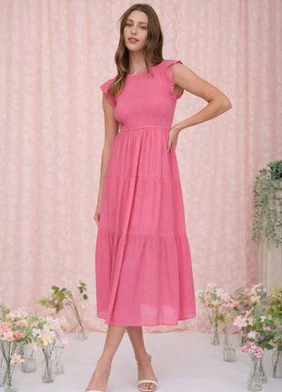 Woman wearing a pink dress standing in front of a pink curtain with floral decorations.