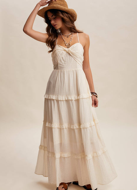 Woman wearing a white tiered dress and straw hat on a plain background