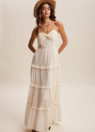 Woman wearing a white tiered dress and straw hat on a plain background
