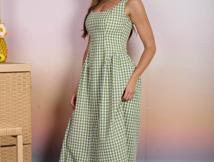 Woman wearing a green checkered dress standing against a blurred beach background
