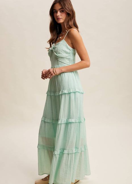 Woman wearing a light green tiered dress against a plain background
