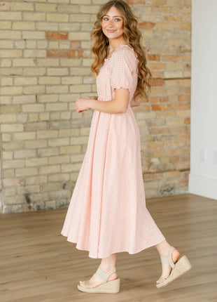 Woman wearing a pink dress standing in front of a brick wall.