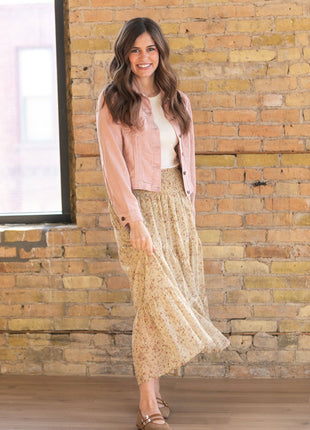 Woman in a pink jacket and beige skirt standing against a brick wall.