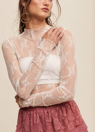 Woman wearing a sheer lace top over a white crop top with a pink skirt on a beige background