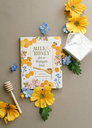 Book titled 'Milk & Honey for a Woman's Soul' surrounded by flowers and a honey dipper on a beige background