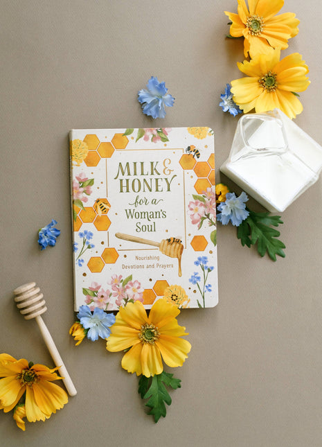 Book titled 'Milk & Honey for a Woman's Soul' surrounded by flowers and a honey dipper on a beige background