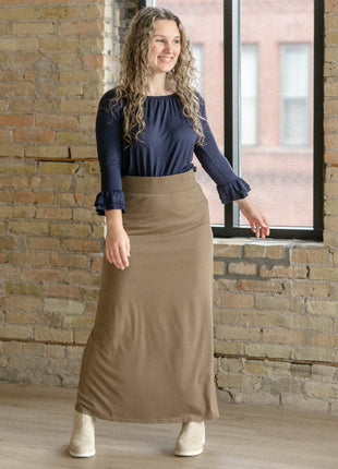 Woman wearing a navy top and brown skirt standing in front of a brick wall.