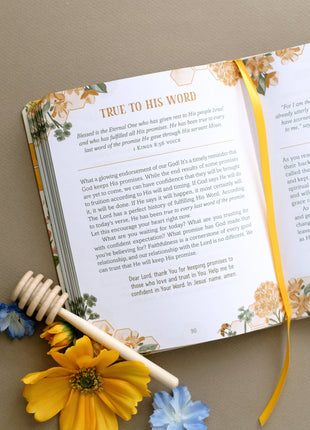 Open book with floral design on a beige surface, accompanied by a honey dipper and flowers.