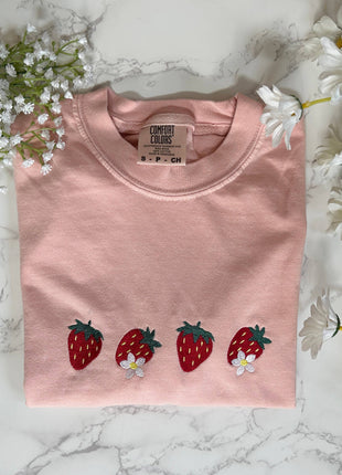 Pink shirt with strawberry designs on a marble surface with flowers