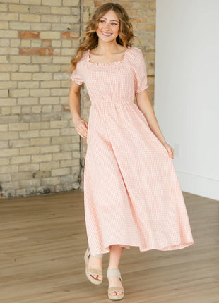 Woman wearing a pink dress standing in a room with wooden flooring and a brick wall.