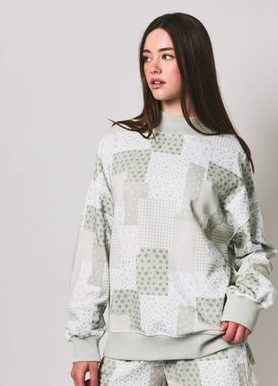 Woman wearing a light green patchwork sweater and shorts on a plain background