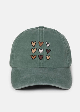 A dusty green baseball cap featuring embroidered hearts in various colors (brown, beige, white, dark red) arranged in a grid on the front, set against a plain light gray background.