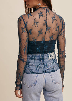 Person wearing a sheer long-sleeve top with floral patterns and light blue jeans on a beige background