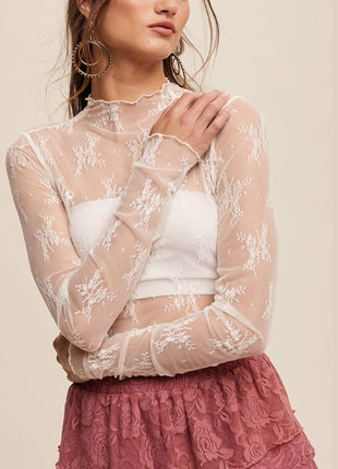Woman wearing a sheer lace top over a white crop top with a pink skirt on a beige background
