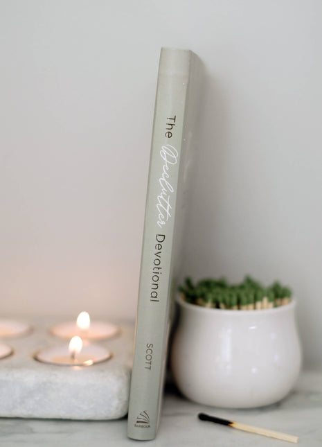 Book titled 'The Devotional' on a surface with candles and a plant in the background