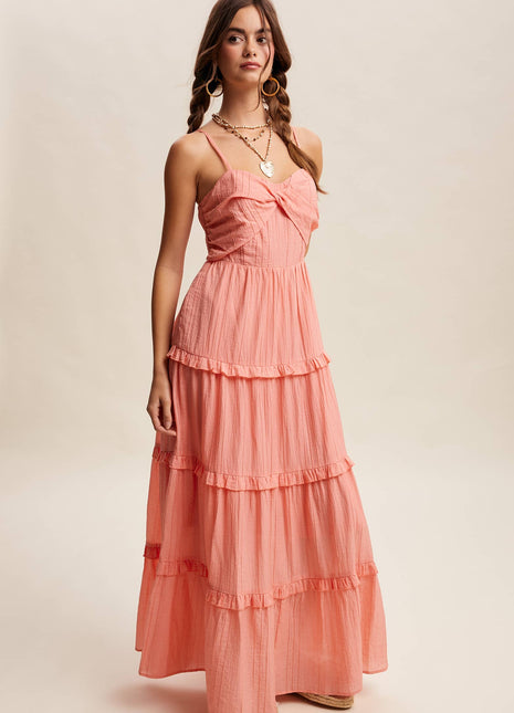 Woman wearing a coral pink dress with ruffled layers on a beige background