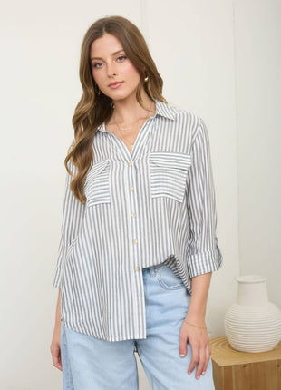 Woman wearing a striped shirt and light blue jeans standing against a white wall.