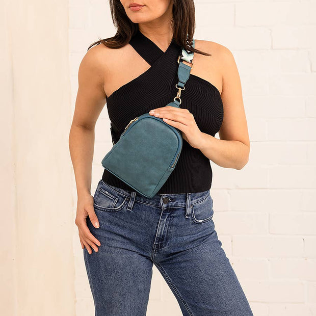 Woman holding a teal waist bag against a white brick wall