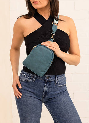 Woman holding a teal waist bag against a white brick wall