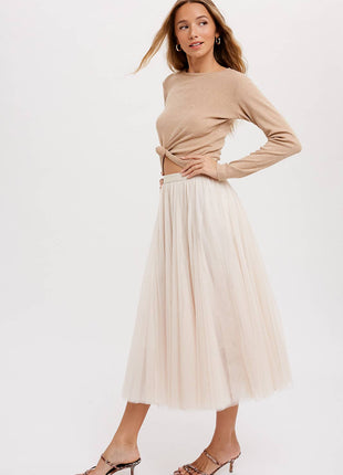Woman wearing a beige long-sleeve top and cream pleated skirt on a white background