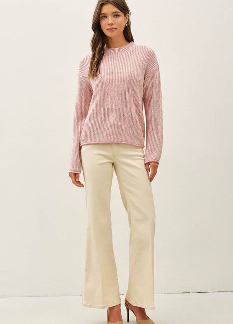 A woman modeling a light pink ribbed knit sweater and cream-colored flared pants against a plain white studio background.